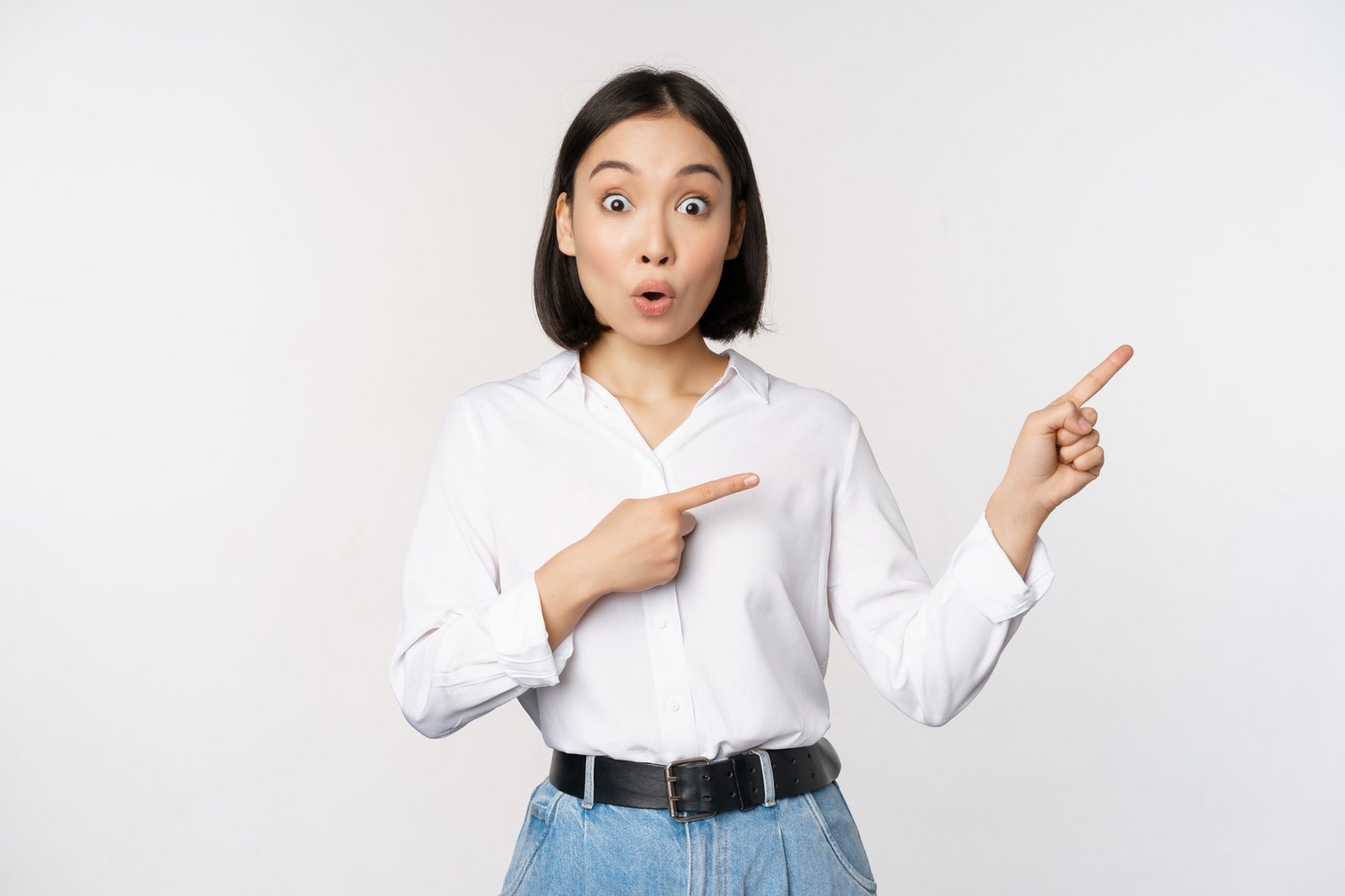 Surprised young woman pointing fingers right. Asian girl showing banner and looking enthusiastic, interested in advertising, standing over white background